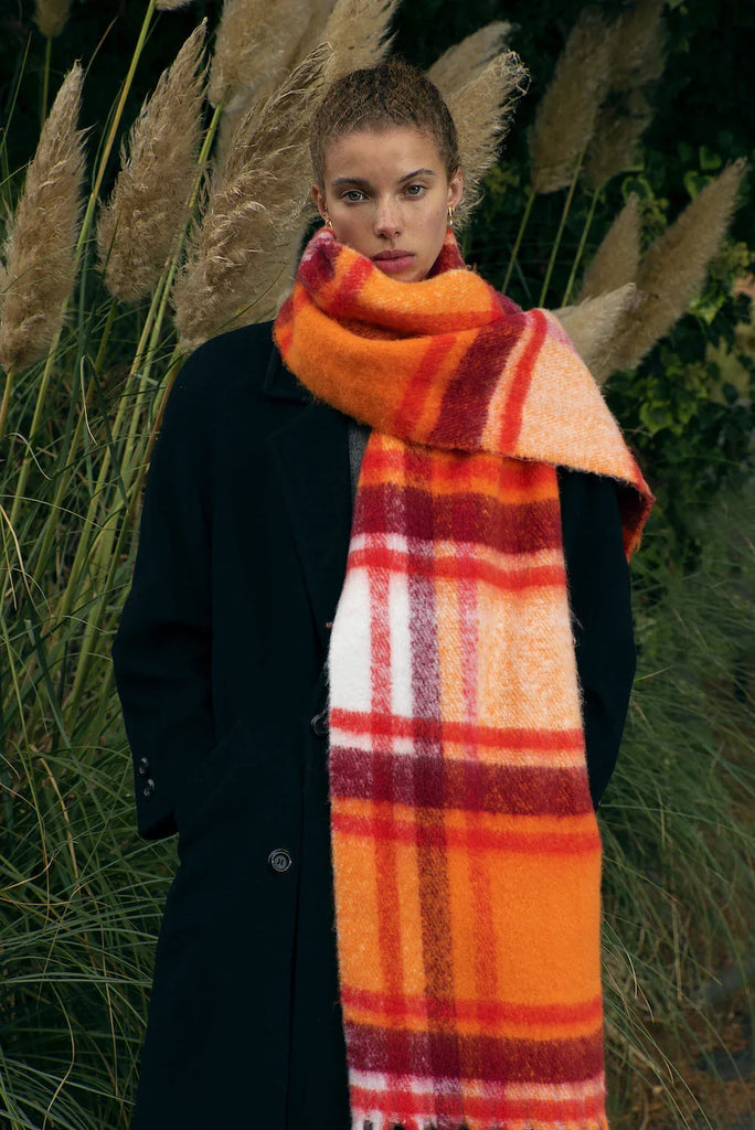woman wearing large orange plaid scarf in front of plants